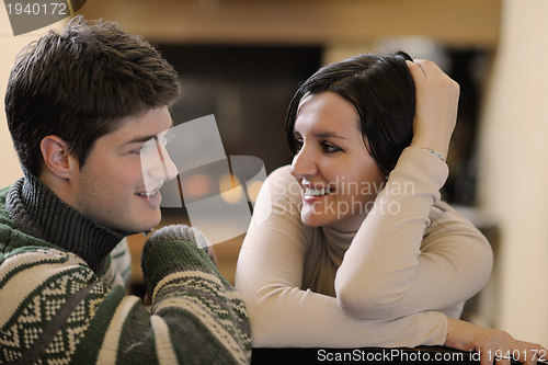 Image of Young romantic couple sitting on sofa in front of fireplace at h