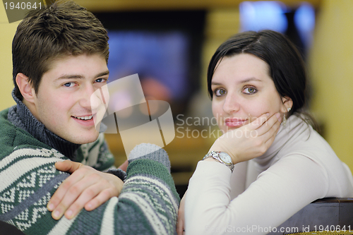 Image of Young romantic couple sitting on sofa in front of fireplace at h