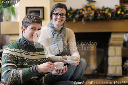 Image of Young romantic couple sitting on sofa in front of fireplace at h