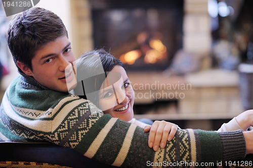 Image of Young romantic couple sitting on sofa in front of fireplace at h