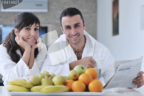 Image of Happy couple reading the newspaper in the kitchen at breakfast