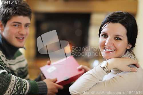 Image of Young romantic couple sitting on sofa in front of fireplace at h