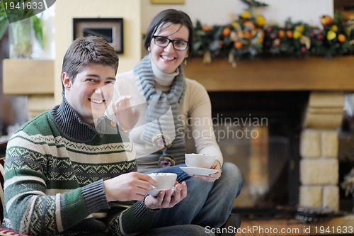 Image of Young romantic couple sitting and relaxing in front of fireplace