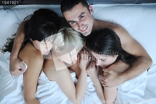 Image of Young handsome man lying in bed with three girls