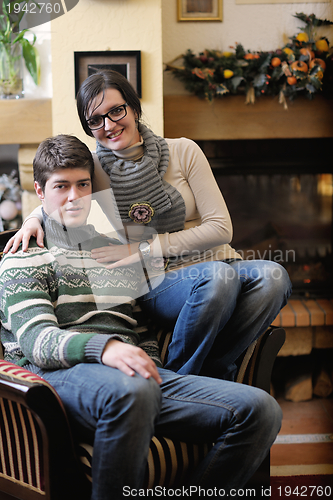 Image of Young romantic couple sitting on sofa in front of fireplace at h