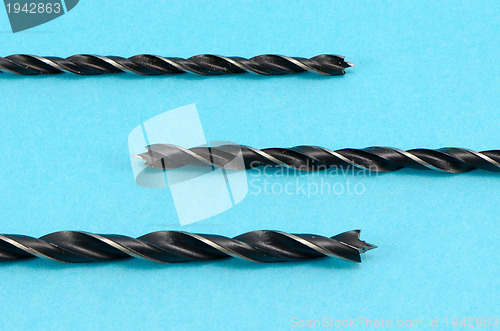 Image of closeup of metal drill bits for wood on blue 