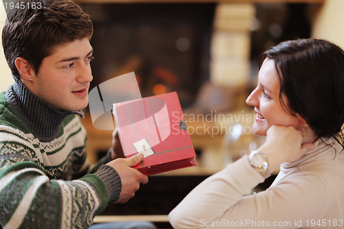 Image of Young romantic couple sitting on sofa in front of fireplace at h