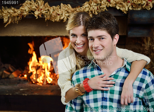 Image of Young romantic couple sitting on sofa in front of fireplace at h