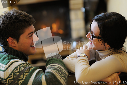 Image of Young romantic couple sitting on sofa in front of fireplace at h