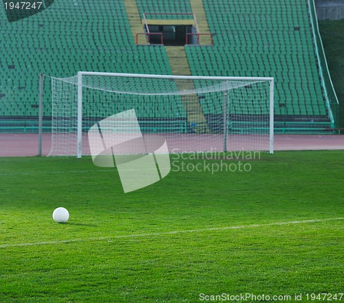 Image of Soccer ball on grass at goal and stadium in background