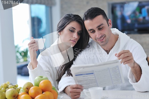 Image of Happy couple reading the newspaper in the kitchen at breakfast
