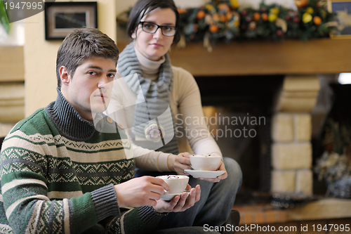 Image of Young romantic couple sitting on sofa in front of fireplace at h