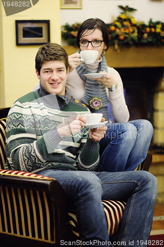 Image of Young romantic couple sitting on sofa in front of fireplace at h