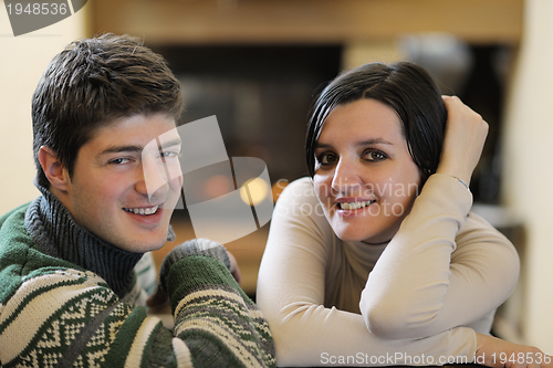 Image of Young romantic couple sitting on sofa in front of fireplace at h