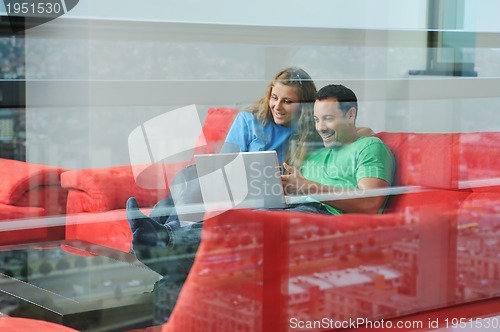 Image of happy couple have fun and work on laptop at home on red sofa