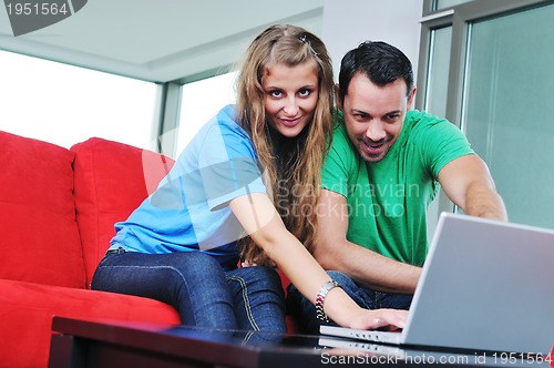 Image of happy couple have fun and work on laptop at home on red sofa