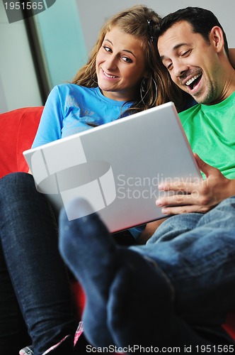 Image of happy couple have fun and work on laptop at home on red sofa