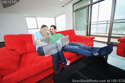 Image of happy couple have fun and work on laptop at home on red sofa