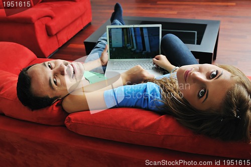 Image of happy couple have fun and work on laptop at home on red sofa