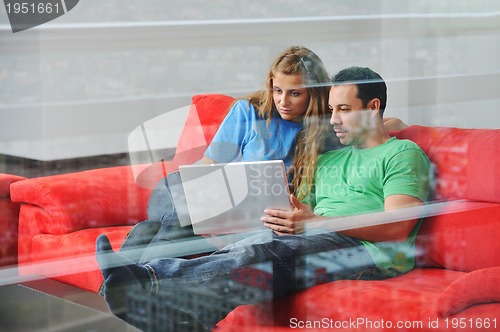 Image of happy couple have fun and work on laptop at home on red sofa