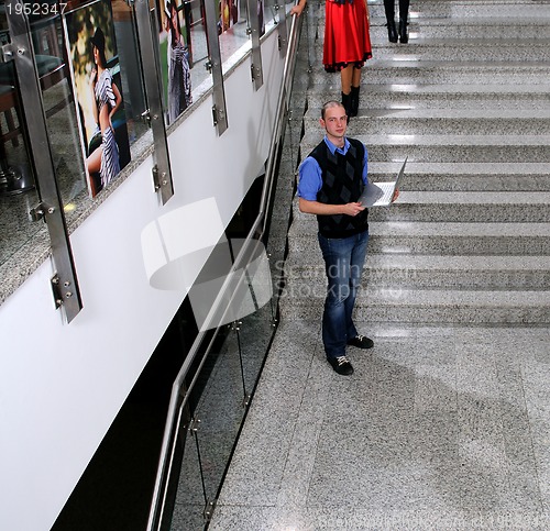 Image of young business man standing on stairs and hold laptop