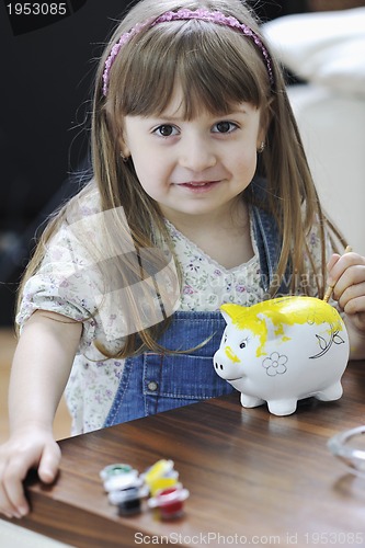 Image of cute little girl painting piggy bank