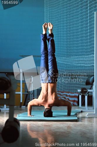 Image of Young man performing  handstand in fitness studio