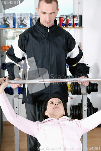 Image of .man assisting woman weitght lifting at a gym 