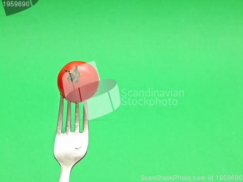 Image of fresh tomato on fork with green background