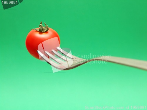 Image of fresh tomato on fork with green background