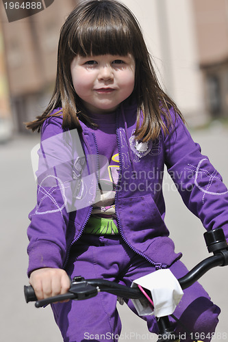 Image of cute little girl driving bicyle at sunny day