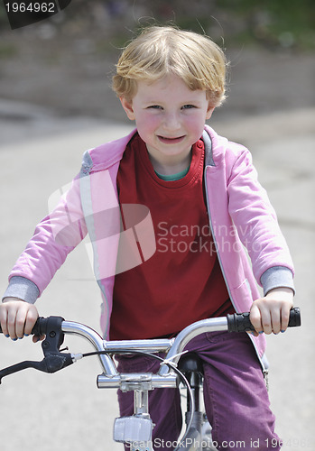 Image of cute little girl driving bicyle at sunny day