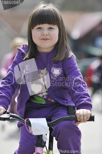 Image of cute little girl driving bicyle at sunny day