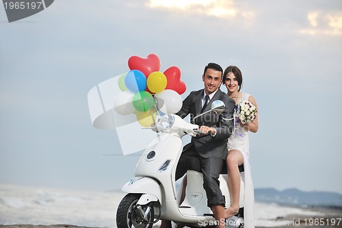 Image of just married couple on the beach ride white scooter