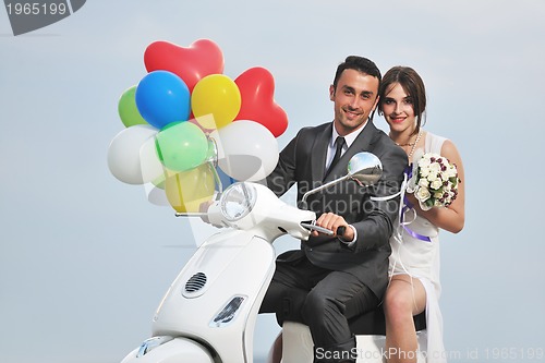 Image of just married couple on the beach ride white scooter