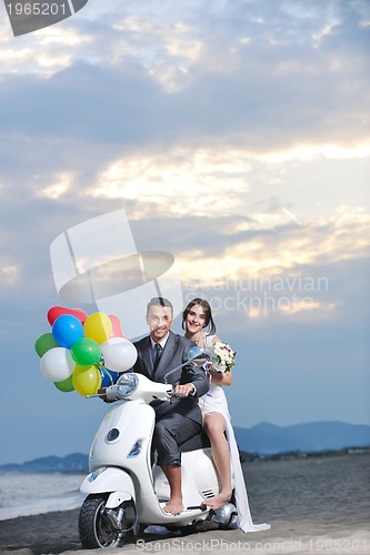 Image of just married couple on the beach ride white scooter