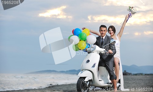 Image of just married couple on the beach ride white scooter