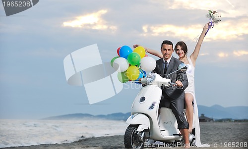 Image of just married couple on the beach ride white scooter