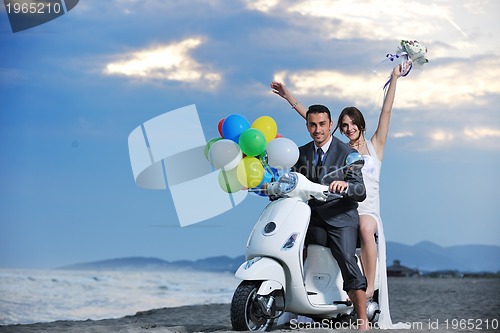 Image of just married couple on the beach ride white scooter