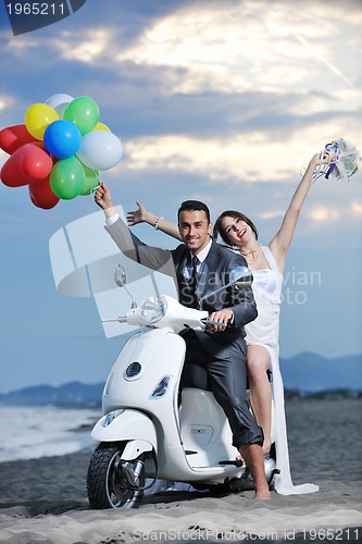 Image of just married couple on the beach ride white scooter