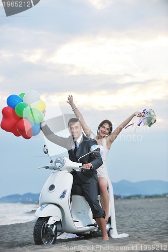 Image of just married couple on the beach ride white scooter