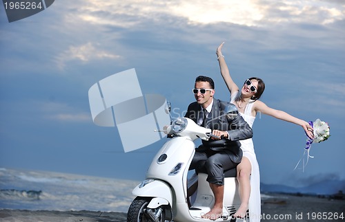 Image of just married couple on the beach ride white scooter