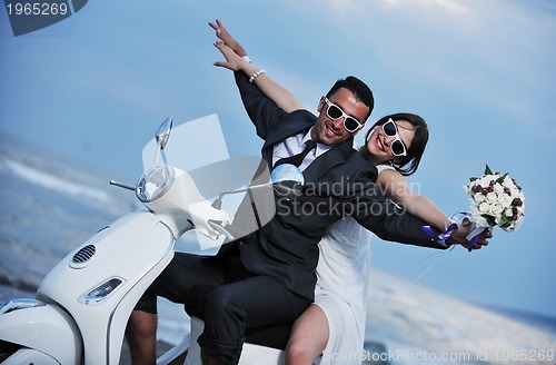 Image of just married couple on the beach ride white scooter