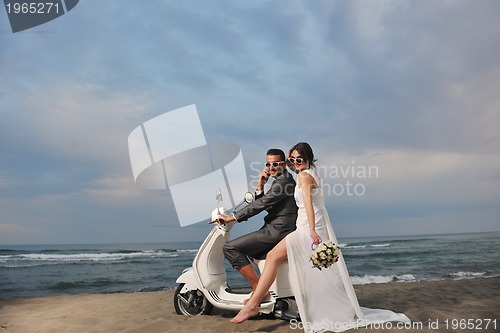 Image of just married couple on the beach ride white scooter