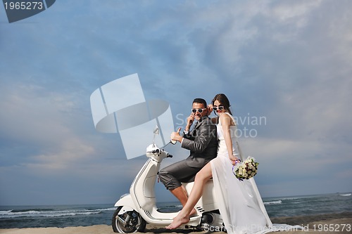 Image of just married couple on the beach ride white scooter