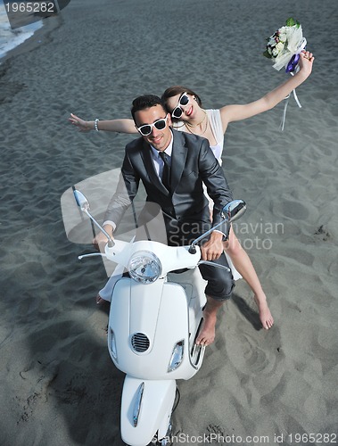 Image of just married couple on the beach ride white scooter