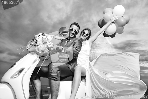 Image of just married couple on the beach ride white scooter