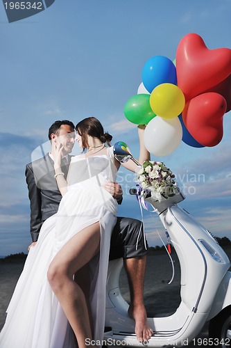 Image of just married couple on the beach ride white scooter