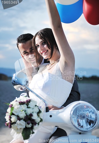 Image of just married couple on the beach ride white scooter