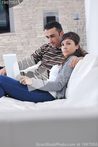 Image of joyful couple relax and work on laptop computer at modern home